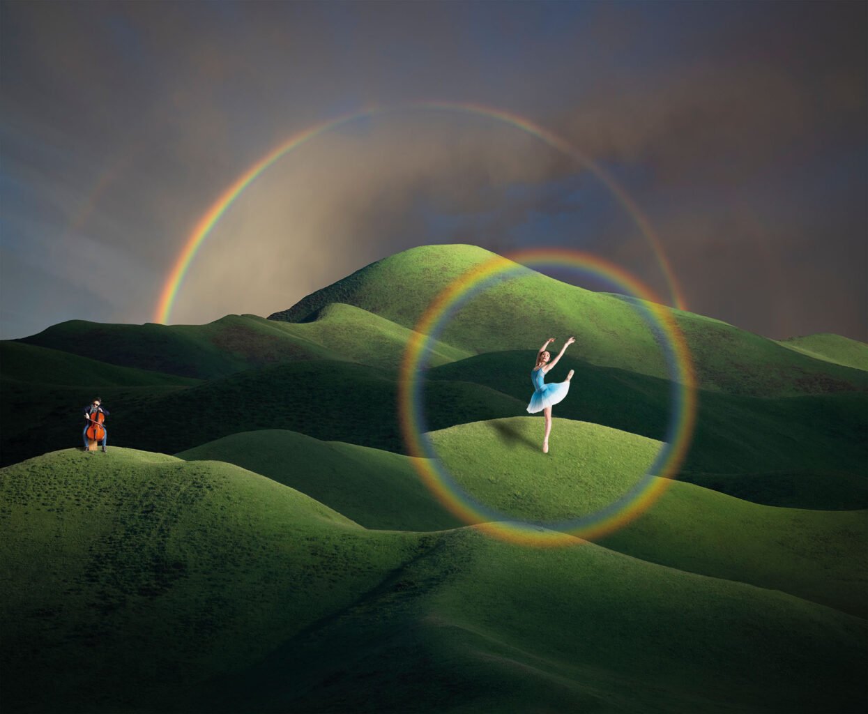 Un paysage de colline verdoyantes sur fond de ciel d'orage. Ce paysage est éclairé par un soleil rasant et par un arc en ciel. Au premier plan, sur une colline, à gauche, une violoncelliste. A droite, sur une colline un peu en retrait, une ballerine sur une pointe semble surgir d'un second arc en ciel qui l'entoure entièrement.